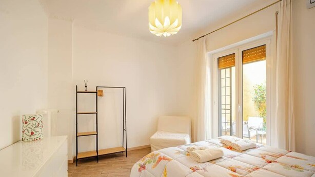 A bedroom with a bed, a chair, a shelf, and a window with curtains. - Appartamento con terrazza vicino S.Pietro (Rome)