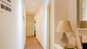 A hallway with wooden flooring, a white wall with text, a lamp, and a mirror. - Appartamento con terrazza vicino S.Pietro (Rome)