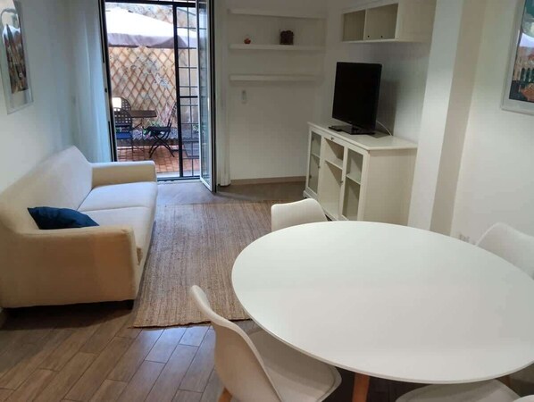 A living room with a sofa, a round table, and a TV on a cabinet.