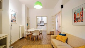 A modern living room with a sofa, a dining table with chairs, a kitchen in the background, and a green pendant light. - Appartamento con terrazza vicino S.Pietro (Rome)