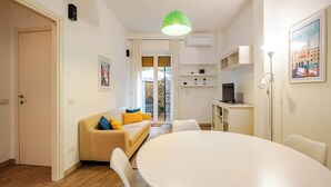 A compact living space with a dining area, a sofa with cushions, a television, and a large window with curtains. - Appartamento con terrazza vicino S.Pietro (Rome)