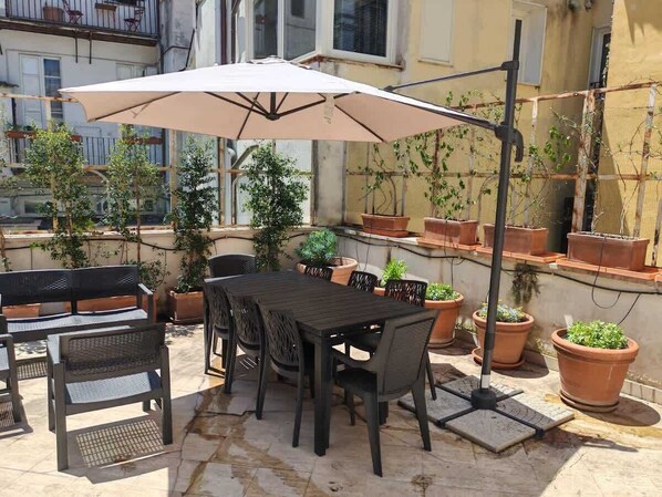 An outdoor patio with a table and chairs, surrounded by potted plants and a large umbrella.