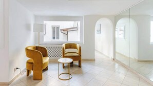 Une pièce moderne avec deux fauteuils jaunes, une petite table ronde et une grande fenêtre donnant sur un escalier.