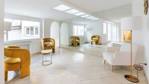 Une pièce spacieuse avec un grand miroir, des chaises jaunes et blanches, et un lampadaire.