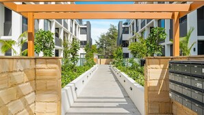 A pathway leading to a modern apartment building with a stone wall on one side and mailboxes on the other. - Allura Bella, Jervis Bay (Huskisson)