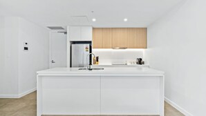A modern kitchen with white cabinetry, a stainless steel sink, and a built-in oven. - Allura Bella, Jervis Bay (Huskisson)