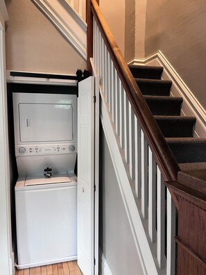 A laundry room with a washer and dryer, a wooden staircase, and a white door. - The Grand Carriage Townhouse (Eau Claire)