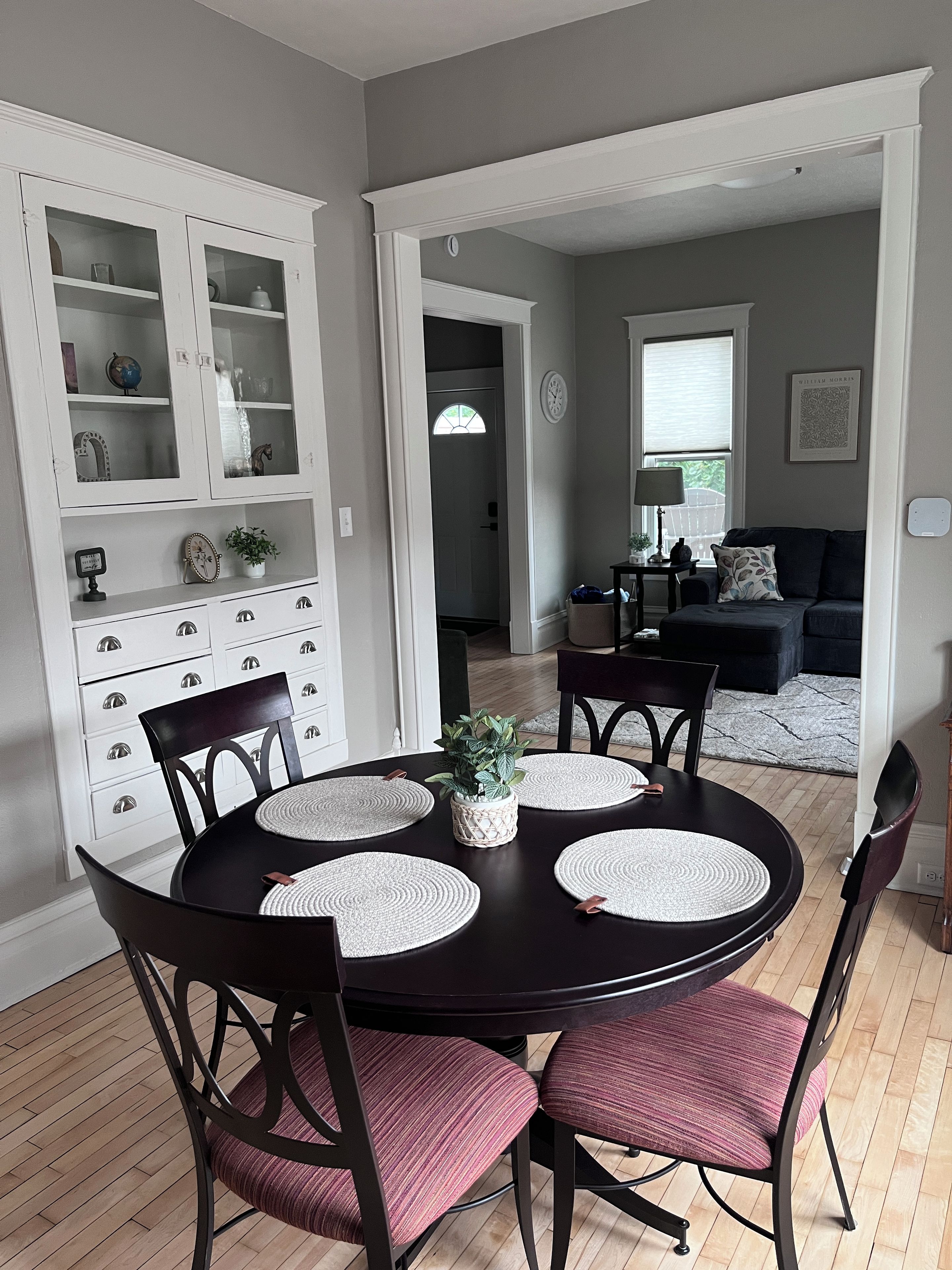 A dining area with a round table, chairs, and a cabinet with glass doors.
