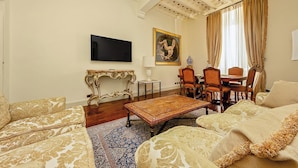 A living room with a sofa, armchair, coffee table, TV, painting, and a dining area with chairs and a table. - Magnifica residenza a Campo de' Fiori (Rome)