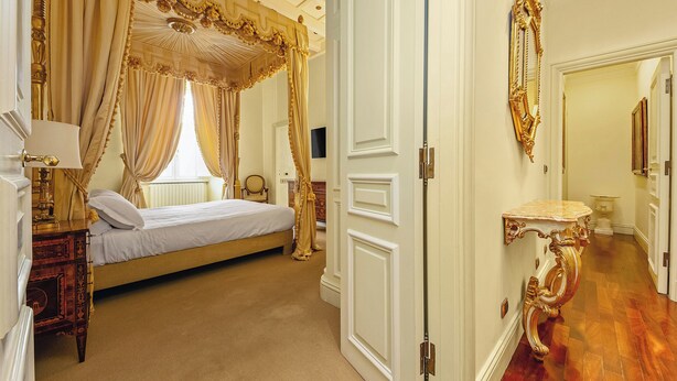Un dormitorio lujoso con una cama con dosel, una mesita de noche con lámpara y un espejo grande en la pared.