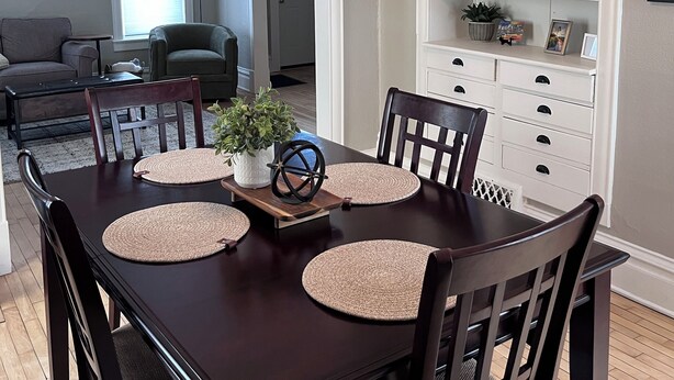 A dining area with a dark wooden table, four chairs, and a white cabinet with glass doors. - The Hudson Carriage Townhouse (Eau Claire)