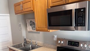 A modern kitchen with wooden cabinets, stainless steel appliances, a double sink, and a granite countertop. - The Hudson Carriage Townhouse (Eau Claire)