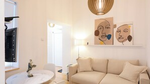 A modern living room with a beige sofa, a round dining table with chairs, a hanging light fixture, and wall art. - Iadra apartment in city center (Zadar)