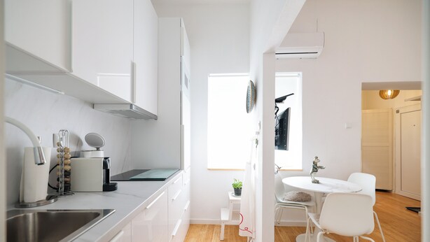 A modern kitchen with white cabinets, a stainless steel sink, and a dining area with a white table and chairs. - Iadra apartment in city center (Zadar)