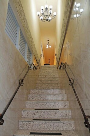 Stunning staircase with a central chandelier and ornate railings, leading to a landing with a door.