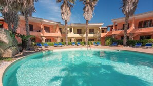 Una piscina circondata da lettini e palme, con un edificio sullo sfondo.