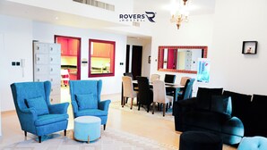 Ein modernes Wohnzimmer mit blauen Sesseln, einem schwarzen Sofa und einem Essbereich mit einer roten Akzentwand.