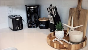 A kitchen counter with a toaster, coffee maker, knife block, wooden cutting board, starfish decoration, pineapple, and a candle.