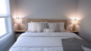 A neatly made bed with white bedding and a grey throw blanket, flanked by two bedside lamps on wooden nightstands.