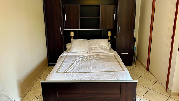 A bedroom with a bed, dark wooden wardrobe, and a nightstand. - Résidence Les Roussets (Jonzac)
