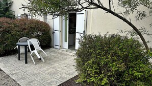 An outdoor patio area with a table and chairs, a door leading to a building, and surrounding greenery. - Résidence Les Roussets (Jonzac)