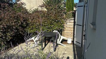 Een terras met een tafel en stoelen, omringd door verschillende planten en een hoge boom.
