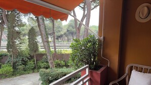 A balcony with a wicker chair, a railing, and a view of trees and a road. - Cozy apartment in Gava Mar. (Gavà)