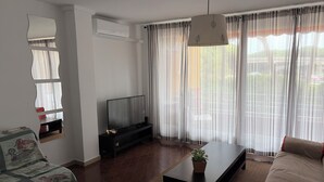A living room with a sofa, a coffee table, a TV, and a window with curtains. - Cozy apartment in Gava Mar. (Gavà)