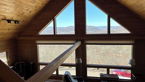 A room with a sloped ceiling, large windows, a sofa, a lamp, and a view of a red car outside. - Escape to a one-of-a-kind Mountaintop Retreat with panoramic westerly views (New Milford)
