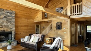 A cozy cabin interior with a stone fireplace, leather furniture, a wooden staircase, and a balcony. - Escape to a one-of-a-kind Mountaintop Retreat with panoramic westerly views (New Milford)