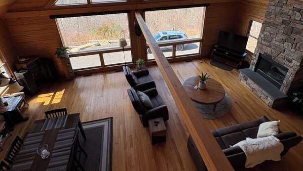 A spacious loft-style room with a high ceiling, a stone fireplace, and large windows offering a mountain view. - Escape to a one-of-a-kind Mountaintop Retreat with panoramic westerly views (New Milford)