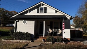 A single-story house with a front porch, a small front yard, and an American flag. - Cute home with fenced backyard, firepit & swings. Near downtown. Pet-friendly! (Kannapolis)
