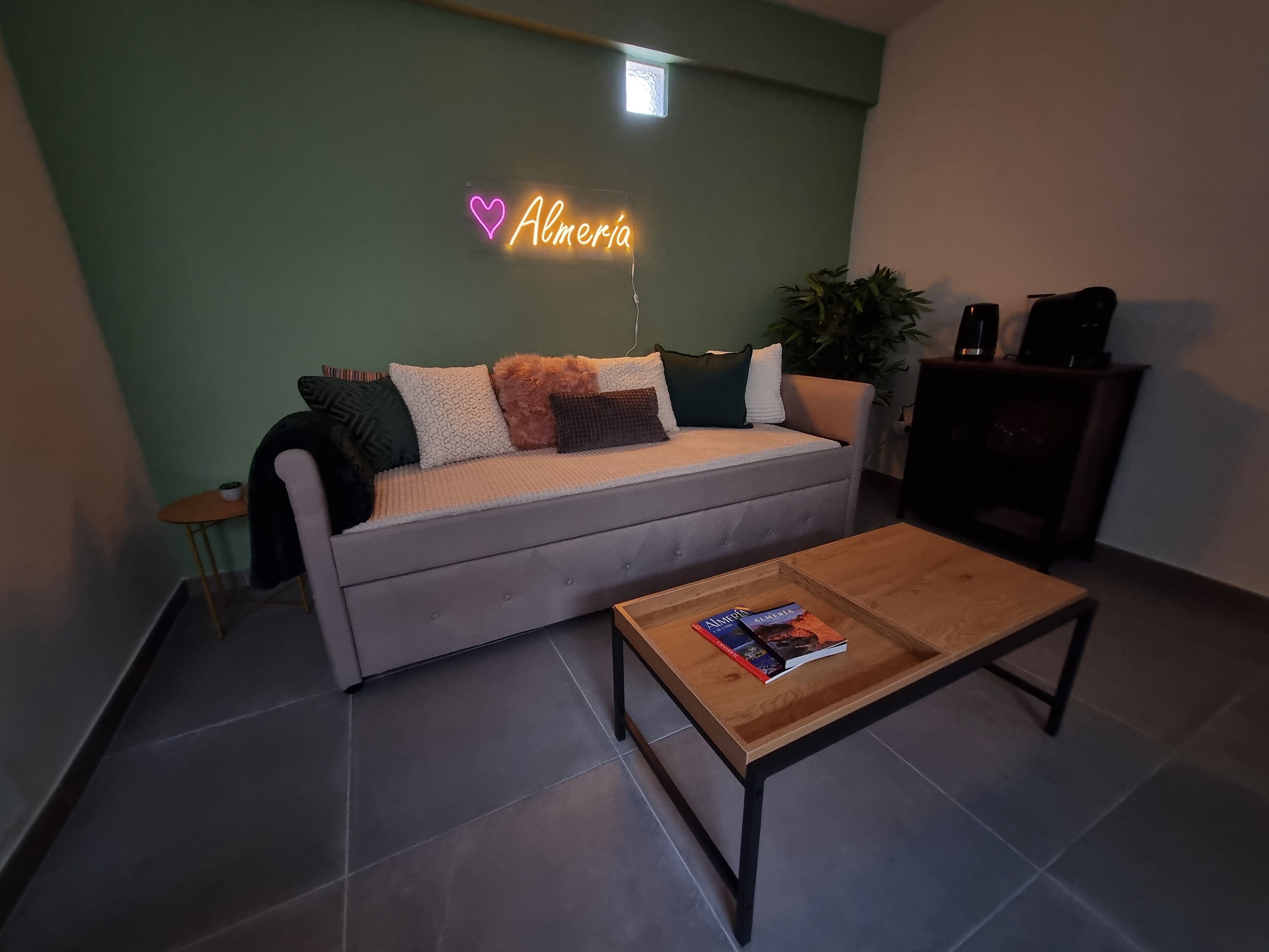 A living room with a grey sofa, a wooden coffee table, and a neon sign on the wall.