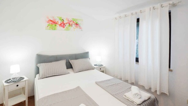 Ein Schlafzimmer mit einem Bett, zwei Nachttischen, einem Fenster mit Vorhängen und einem Wandbild.