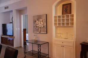 A living room with a TV, a glass coffee table, a painting, and a shelving unit with vases. - 2BD Estrella del Mar in Mazatlan (Mazatlán)