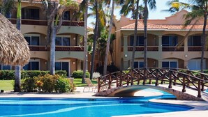 Area piscina di un resort con un ponte, palme e un edificio con balconi.