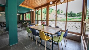A dining area with a wooden table and colorful chairs, large windows with a view of greenery and a building outside. - latour Mestia (Mestia)