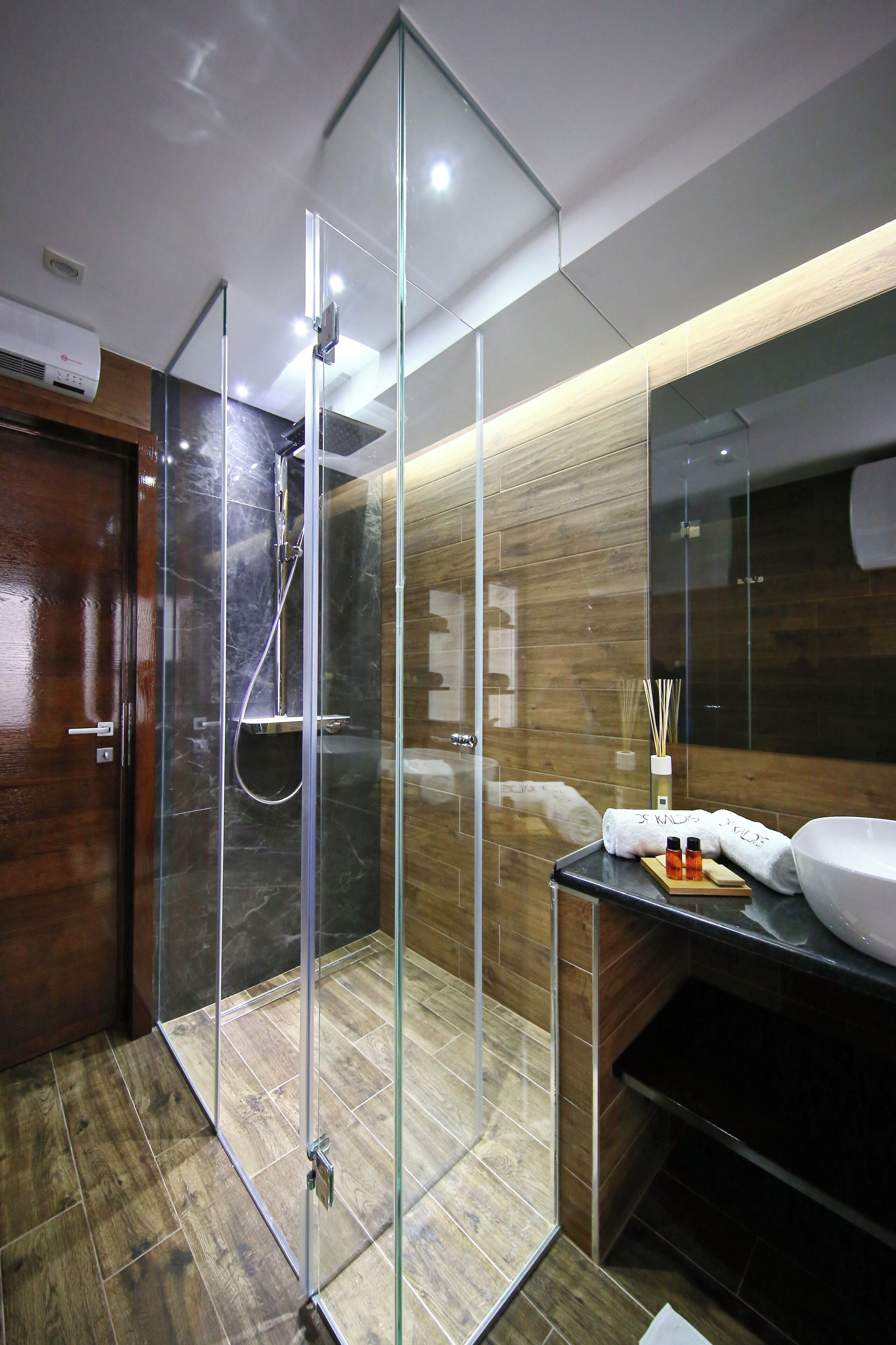 A modern bathroom with a glass-enclosed shower, wooden flooring, and a vanity with a mirror and towel.