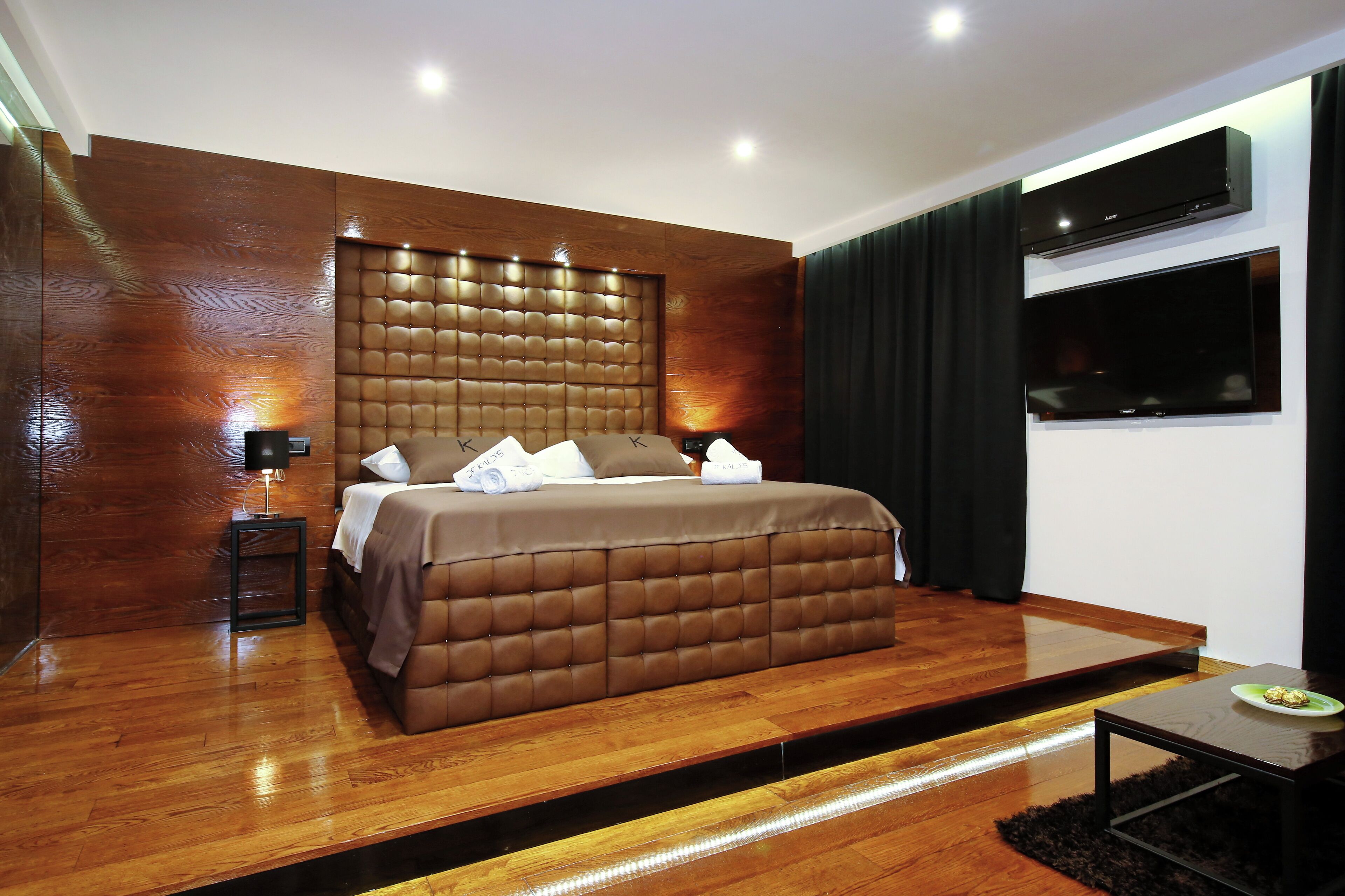 A modern bedroom with a large bed, a flat-screen TV, and a wooden floor.