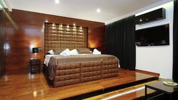 A modern bedroom with a large bed, a flat-screen TV, and a wooden floor.