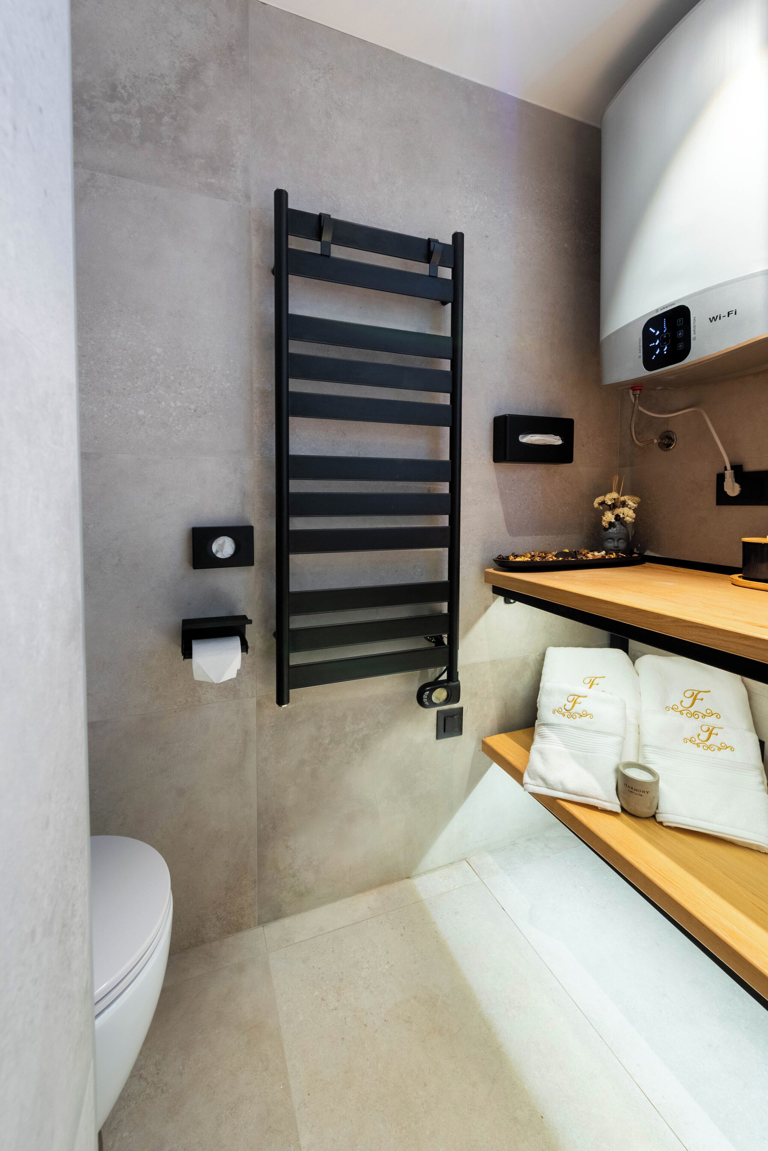 A modern bathroom with a towel rack, a toilet, a sink with a mirror, and a wall-mounted heater.