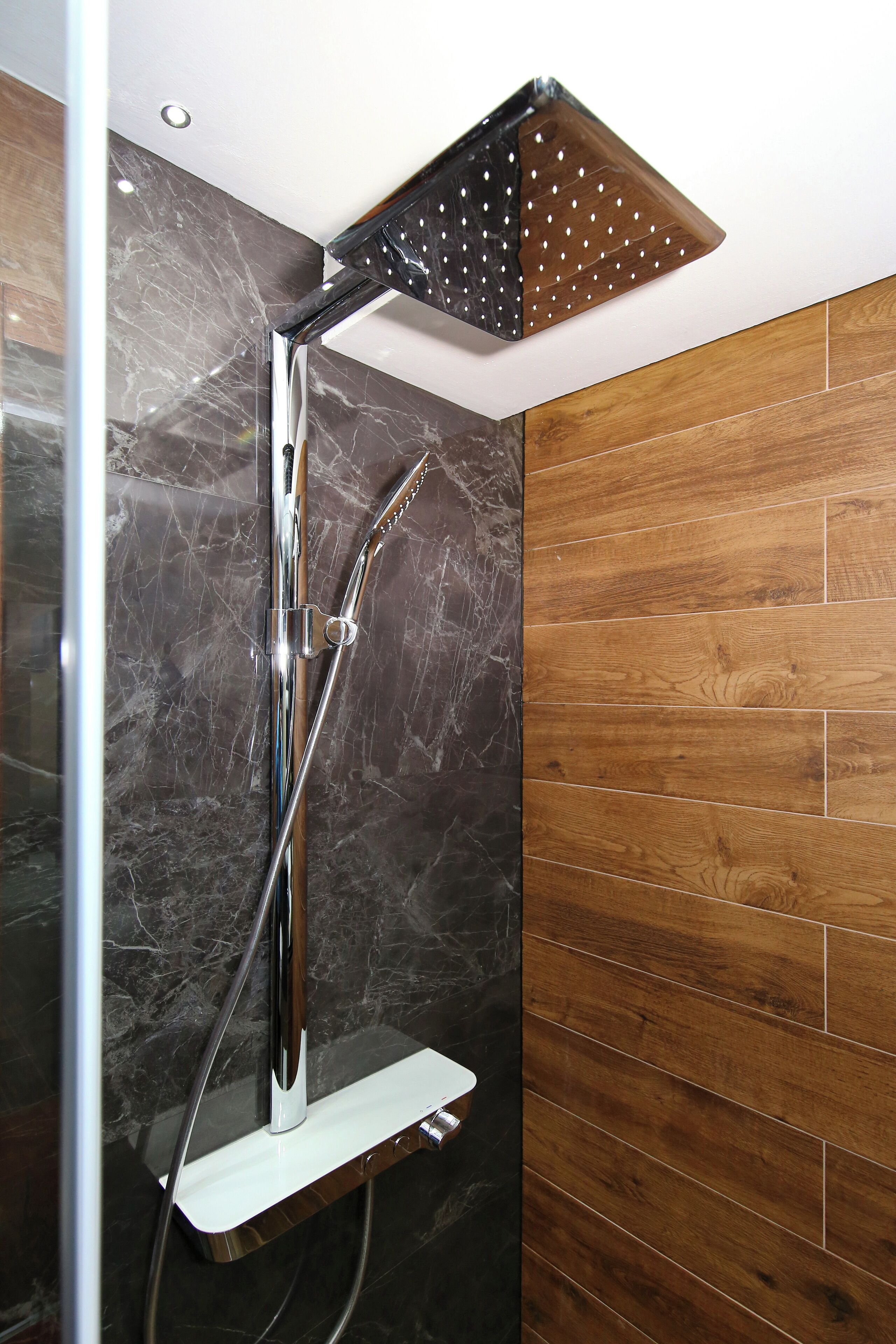 A modern shower with a chrome finish, a wooden panel wall, and a marble-like backsplash.