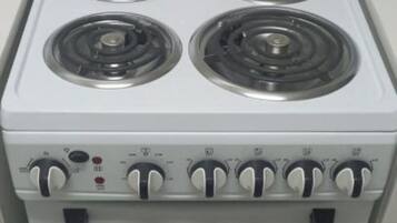 Una estufa blanca con cuatro hornillas, un panel de control con perillas y un horno integrado.
