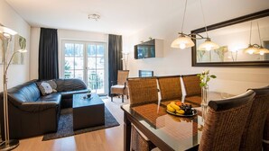 A modern living room with a sofa, dining table, and chairs. There is a large window with curtains, a flat-screen TV, and a mirror on the wall. - Apartment in Bad Gastein Near Ski Lifts (Bad Gastein)