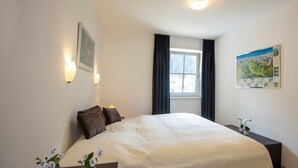 A neatly arranged bedroom with a large bed, bedside tables, a window with curtains, wall-mounted lights, and a map on the wall. - Apartment in Bad Gastein Near Ski Lifts (Bad Gastein)