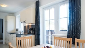 A modern kitchen with white cabinets, a dining table with chairs, and a fruit plate on the table. - Apartment in Salzburg Near Ski-lift (Bad Gastein)