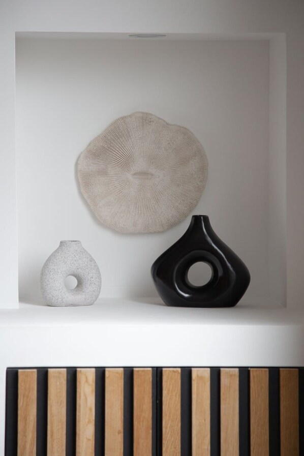 A white shelf with three decorative objects: a textured round wall piece, a grey vase, and a black vase.