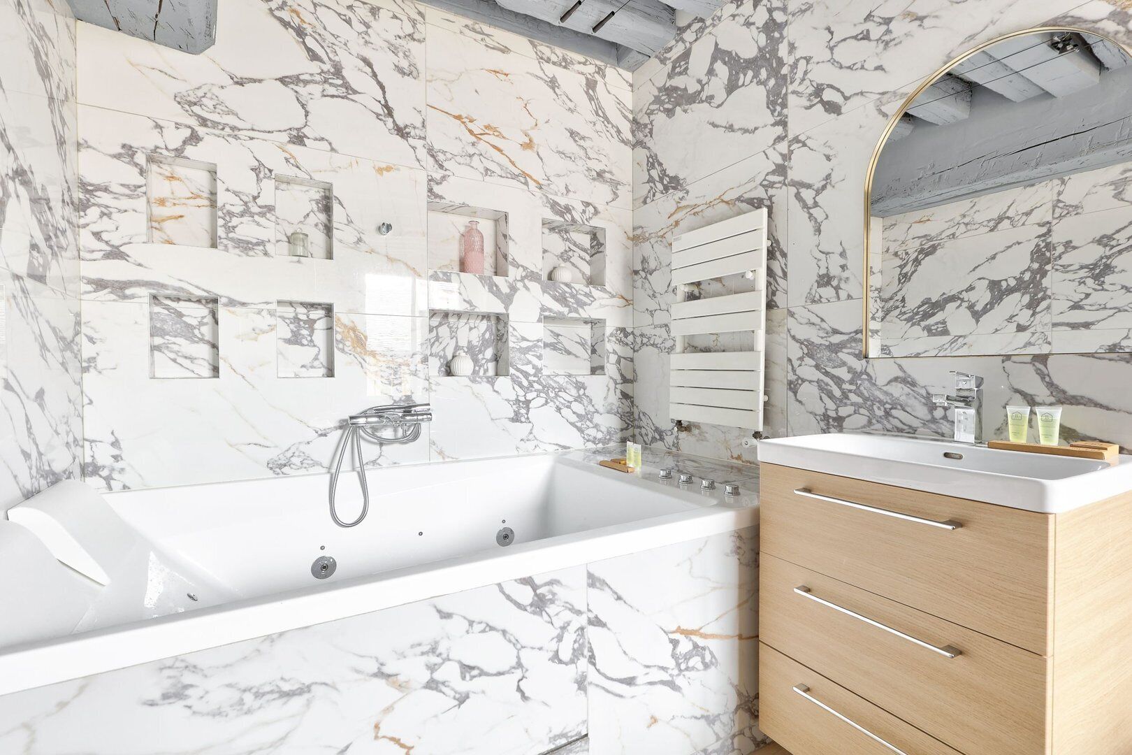 A modern bathroom with a marble backsplash, a freestanding bathtub, a vanity with a mirror, and a wooden cabinet.