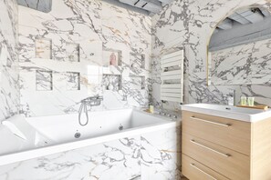Un baño moderno con salpicadero de mármol, una bañera independiente, un tocador con espejo y un armario de madera.