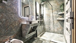 A modern bathroom with a walk-in shower, a bidet, and a marble-tiled wall.
